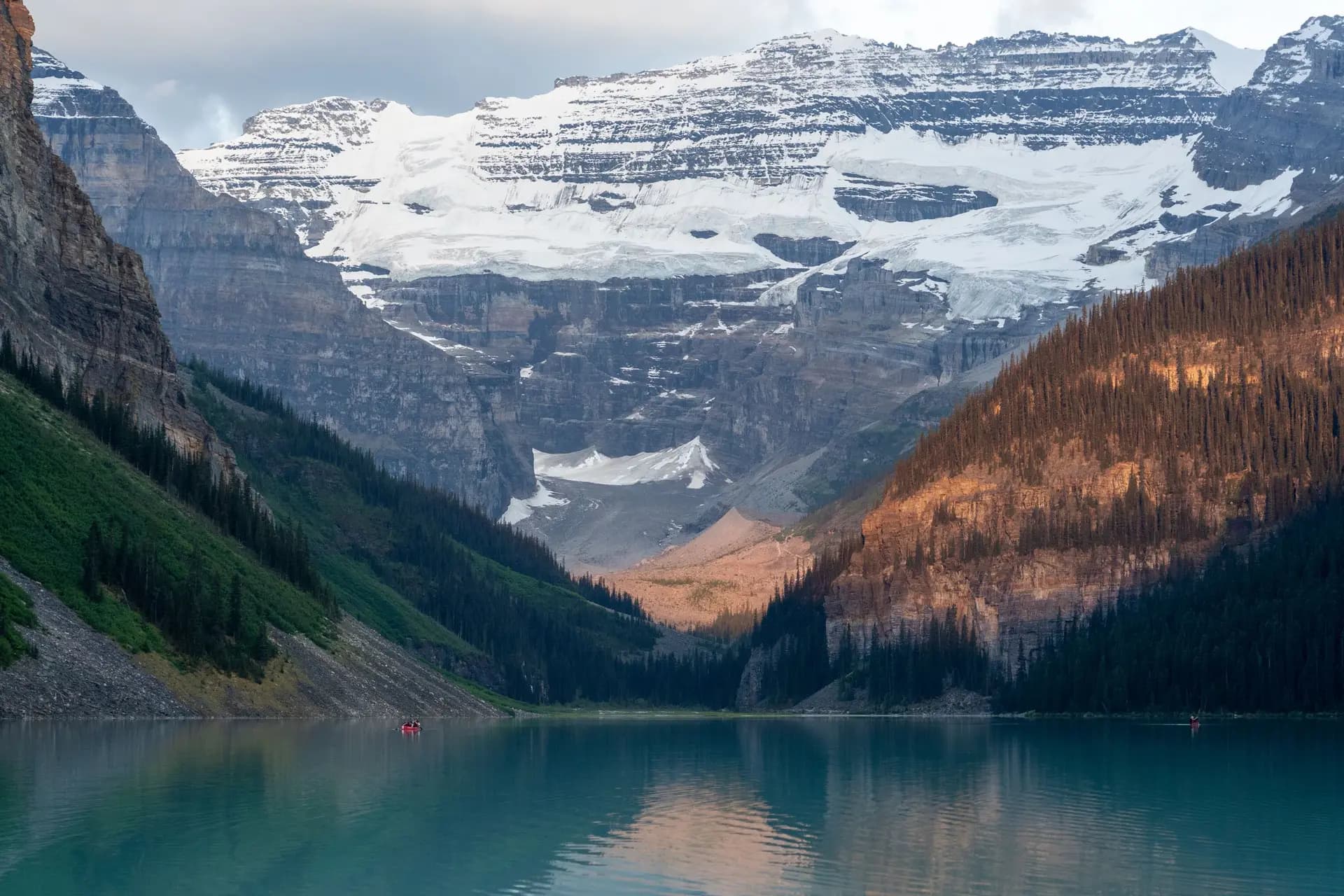 Turquoise water at Lake Louise in Banff, with a red canoe by the shore and snow on the peaks.