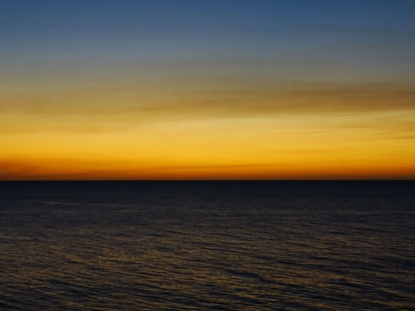 The sun setting on the Caribbean Sea at Negril, Jamaica, with clouds over calm water.