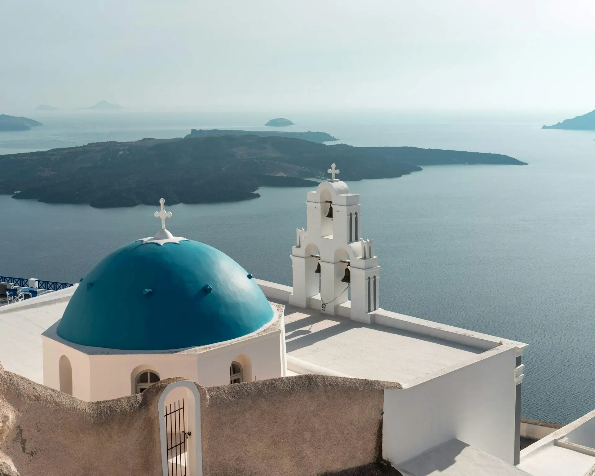 White buildings and a blue dome above the sea in Santorini, with the caldera in the distance.