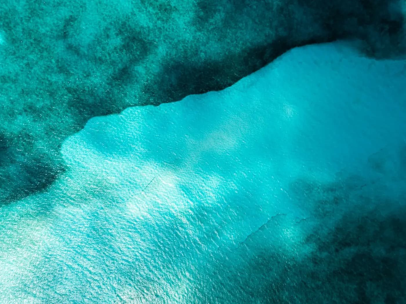 Turquoise water meeting white sand at Cancun, seen from above, with a small boat near the beach.