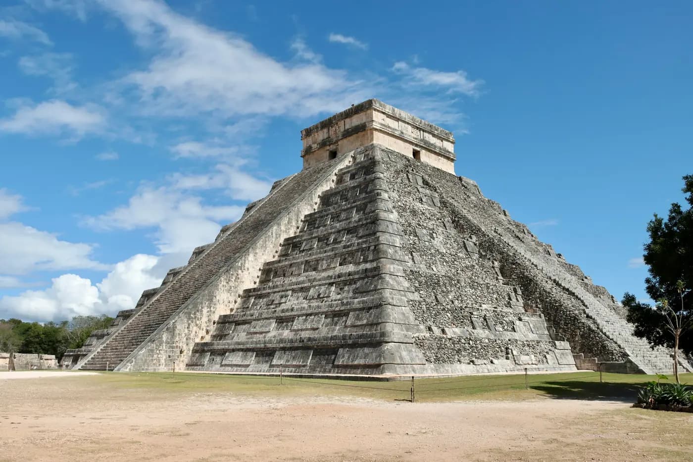 El Castillo, the stone step pyramid at Chichen Itza, in a green field under a blue sky.