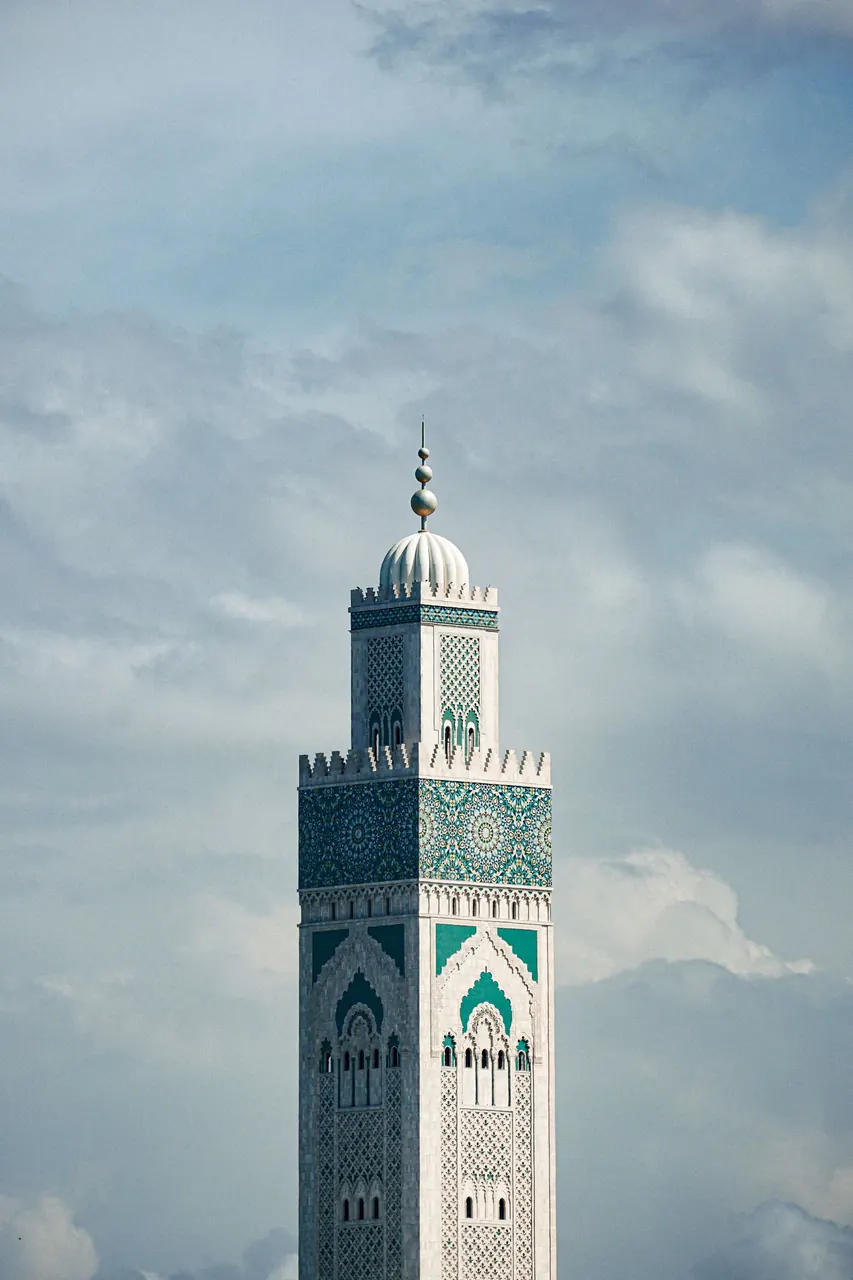 The minaret of the Hassan II Mosque in Casablanca against a cloudy sky.