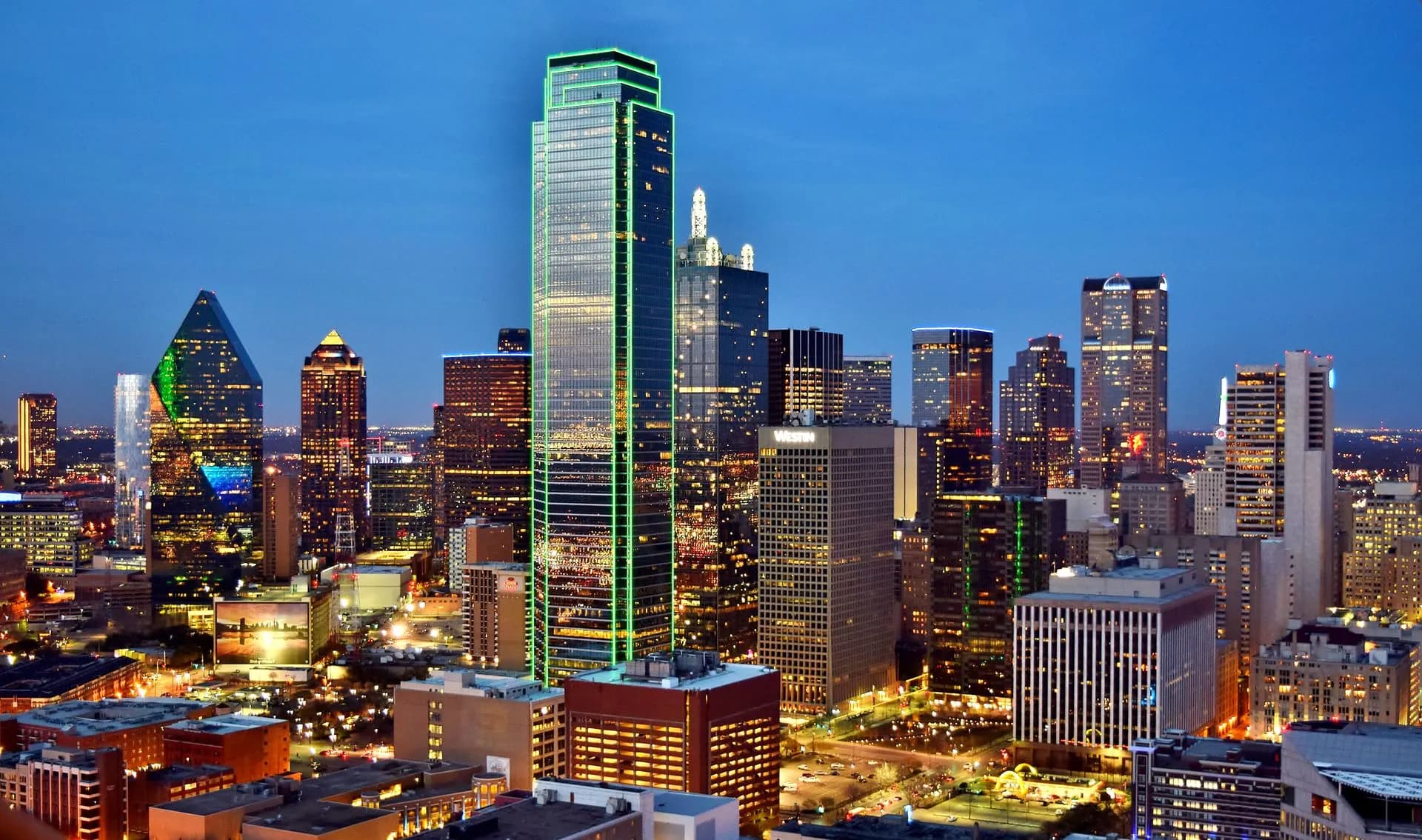 Downtown Dallas at night, with the green-lit Bank of America Plaza above the city.