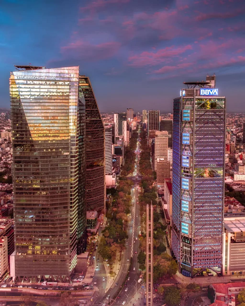 Skyscrapers along Paseo de la Reforma in Mexico City under a pink sunset sky.