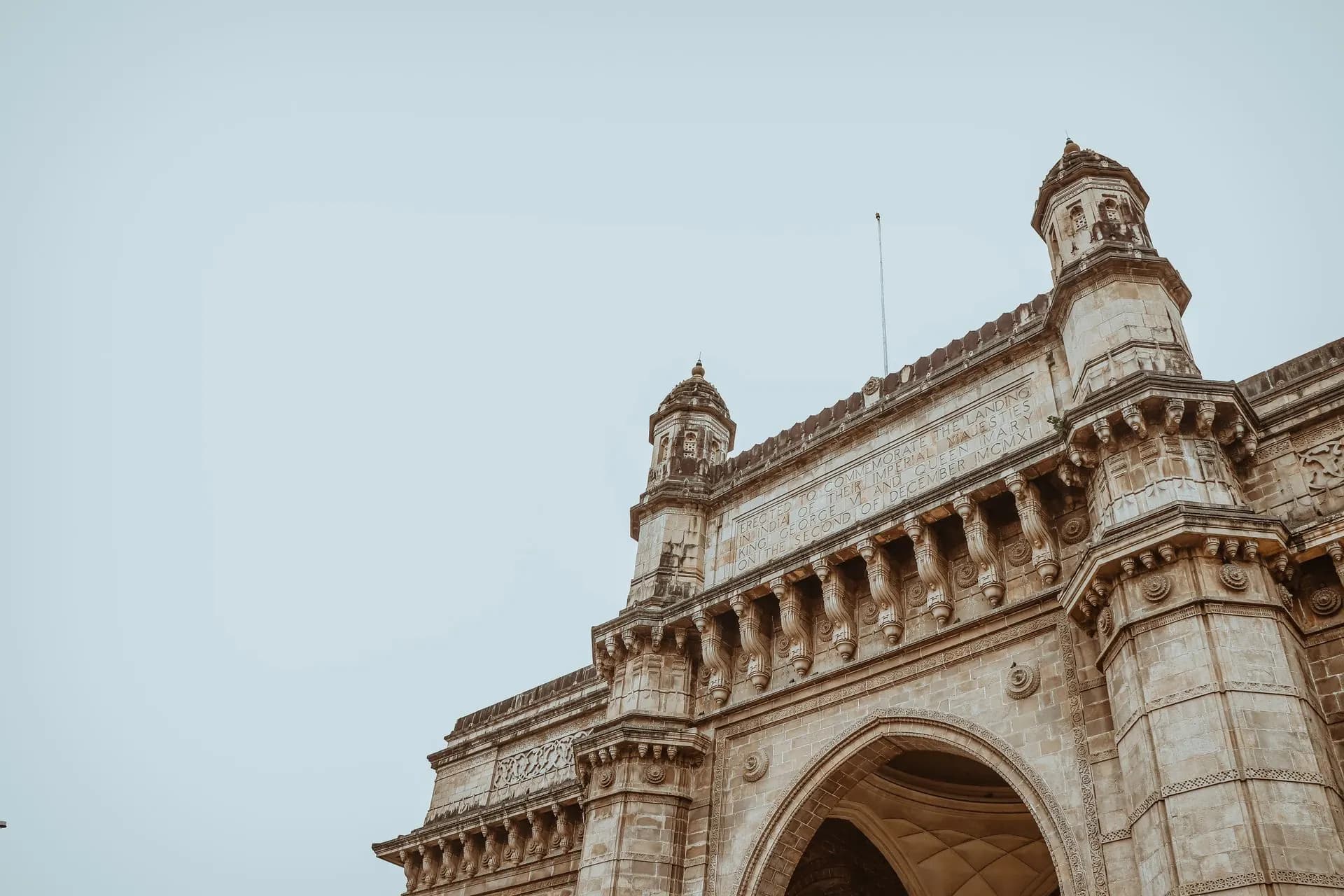 The Gateway of India in Mumbai, seen from below against a pale sky.